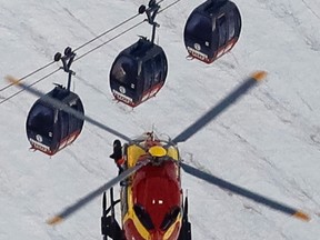 An EC-135 helicopter operated by the French Societe' Civile hovers, Friday, Sept. 9, 2016, near three cars of the Panoramic Mont Blanc cable car where tourists were trapped after it stalled around 4 p.m. (1400 GMT) on Thursday, when its cables reportedly tangled. (AP Photo/Luca Bruno)