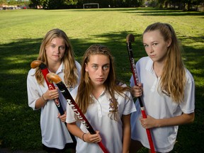 Claire Adams, left, Jayden Alp, and Tay Barnabe, members of the championship-defending Nepean High School varsity field hockey team, pose for a photo at their school's field where they may have to play this season because the city of Ottawa has decided to charge hourly rental fees for the premium artificial turf at Minto Field. The head coach Brian Lee is upset because playing on natural grass jeopardizes the safety of the girls.