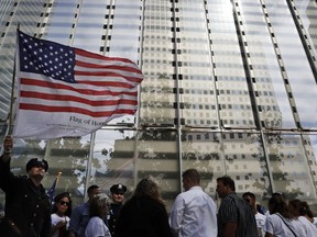 Police officer Eloy Suarez holds an American flag with the names of the people who died during the attacks on the World Trade Center during a 15th anniversary ceremony of the terrorist attack, while standing on the outskirts of the Sept. 11 memorial, Sunday, Sept. 11, 2016, in New York. (AP Photo/Mary Altaffer)