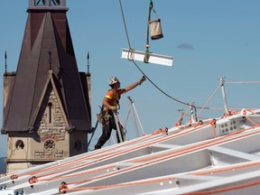 A worker reaches for a steel beam being lowered by crane into place on the roof of West Block as renovations continue Thursday. Adrian Wyld /CP