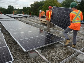 London District Renewable Energy Co-operative board members Kyle McIntyre, left, and Cody Young install solar panels on the roof of a strip mall in Lambeth this week. (MORRIS LAMONT, The London Free Press)