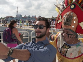 This undated photo provided by Carnival Corporation shows Josh Garcia in Playa del Carmen, Mexico, taking a selfie with a local resident dressed in costume to greet cruise passengers in a scene from a new show airing on NBC this fall called "The Voyager with Josh Garcia." The show is one of three new shows produced by Carnival Corp., showcasing vacation and travel connected to cruising. Josh Garcia hosts the show, which explores the history and culture of various ports through meetings with locals. (Carnival Corporation via AP)