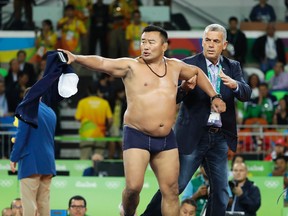 A coach of Mongolia's wrestler Mandakhnaran Ganzorig take off their clothes in protest against the decision of the jury to award the bronze medal to Uzbekistan's Ikhtiyor Navruzov during the men's 65-kg freestyle wrestling competition at the 2016 Summer Olympics in Rio on Aug. 21, 2016. (AP Photo/Markus Schreiber)