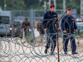 Hungarian policemen patrol along a barbed wire fence in the transit zone at Hungary's southern border with Serbia is seen near Tompa, 169 kms southeast of Budapest, Hungary, Wednesday, Sept. 21, 2016. Hungarian prison inmates have ramped up their production of razor wire, working around the clock as Hungary prepares to build a second fence on the border with Serbia to keep out refugees and other migrants. (Sandor Ujvari/MTI via AP)