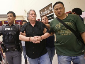 In this Saturday, Sept. 24, 2016 photo, Thai policemen escort a suspect, center, after three men were arrested on charges of trafficking in forged passports and concealing a dismembered body at an apartment in Bangkok, Thailand. Thai police are seeking to identify the corpse found in a freezer when they raided the apartment and arrested two Americans and a Briton. (AP Photo/Sakchai Lalit)