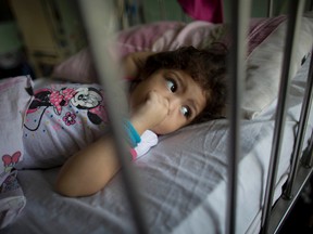 In this Aug. 16, 2016 photo, three-year-old Ashley Pacheco sucks on her thumb as she rests in a hospital bed during her two-month stay at University Hospital in Caracas, Venezuela. As the health care system collapses, the tiniest slips, like Ashley’s tumble while chasing her brother in mid-July, turned into a life-or-death crisis when her scraped knee led to a staph infection. (AP Photo/Ariana Cubillos)
