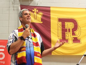 The flag of Regiopolis-Notre Dame Catholic High School hangs on the wall of the gym behind him as Joe Roberts, who is pushing a shopping cart across the country to raise awareness for youth homelessness, addresses students at the school in Kingston. (Michael Lea/The Whig-Standard)