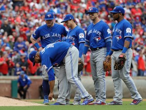 Toronto Blue Jays pitcher Francisco Liriano leans over to grab the rosin bag as, from left rear, Josh Donaldson, Darwin Barney, Troy Tulowitzki and Edwin Encarnacion, right, stand by him after he was hit on the back of the head by a single off the bat of Texas Rangers' Carlos Gomez in the eighth inning of Game 2 of an American League Division Series on Oct. 7, 2016, in Arlington, Texas. (AP Photo/David J. Phillip)