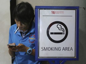 A Filipino smokes by a smoking area sign outside a mall in Manila, Philippines Tuesday, Oct. 11, 2016. Health Secretary Paulyn Ubial said Tuesday she hopes Philippine President Rodrigo Duterte can sign the draft executive order banning smoking in public nationwide before the end of the month. She also said e-cigarettes will be included in the ban. (AP Photo/Aaron Favila)
