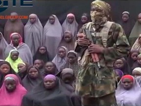 In this undated image taken from video distributed Sunday, Aug. 14, 2016, an alleged Boko Haram soldier standing in front of a group of girls alleged to be some of the 276 abducted Chibok schoolgirls held since April 2014, in an unknown location. (Militant video/Site Institute via AP File)