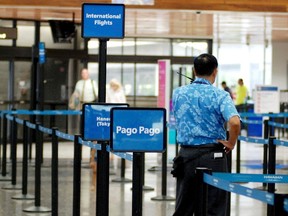 In this Oct. 10, 2016 photo, an airline employee stands next to a sign for where to check-in for Hawaiian Airlines flights to Pago Pago, American Samoa at Honolulu International Airport in Honolulu.(AP Photo/Jennifer Sinco Kelleher)