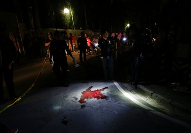 In this Sept. 5, 2016 photo, police inspect the site where alleged drug user Marcelo Salvador was shot dead by unidentified men in Las Pinas, south of Manila, Philippines. Drug dealers and drug addicts, were being shot by police or slain by unidentified gunmen in mysterious, gangland-style murders that were taking place at night. Salvador became a victim, the casualty of a vicious war on drugs that has claimed thousands of lives as part of a campaign by Philippine President Rodrigo Duterte. (AP Photo/Aaron Favila)