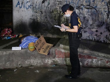In this Sept. 21, 2016 photo, a police investigator checks on the unidentified body of an alleged drug lord with his head, hands and feet wrapped in packaging tape and with a cardboard sign that reads "Kage Lao, Drug Lord of Mindanao, You will be next!" after it was dumped by unidentified men along a dark alley in Manila, Philippines. Bodies had begun turning up in cities all over the Philippines ever since President Rodrigo Duterte launched a controversial war on drugs this year. Drug dealers and drug addicts, were being shot by police or slain by unidentified gunmen in mysterious, gangland-style murders that were taking place at night. (AP Photo/Aaron Favila)