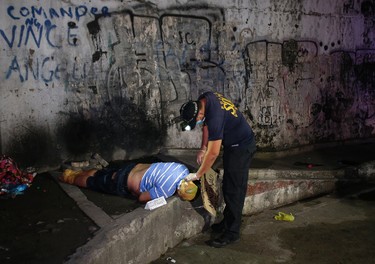 In this Sept. 21, 2016 photo, a policeman checks on the unidentified body of an alleged drug lord with his head, hands and feet wrapped in packaging tape after it was dumped by unidentified men along a dark alley in Manila, Philippines. Bodies had begun turning up in cities all over the Philippines ever since President Rodrigo Duterte launched a controversial war on drugs this year. Drug dealers and drug addicts, were being shot by police or slain by unidentified gunmen in mysterious, gangland-style murders that were taking place at night. (AP Photo/Aaron Favila)