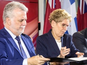 Quebec Premier Philippe Couillard, left, and Ontario Premier Kathleen Wynne pass a document between themselves as they sign an agreement after a joint meeting of cabinet ministers in Toronto on Friday, October 21, 2016. (THE CANADIAN PRESS/Chris Young)