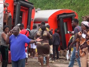 In this image made from video, passengers stand beside derailed train carriages after an accident in Eseka, Cameroon, Friday, Oct. 21, 2016. Cameroon's transport minister says at least 53 people have died after a train overloaded with passengers derailed along the route that links the country's two major cities. (Equinox TV via AP)