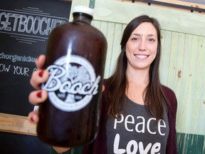 Shannon Slade, co-owner of Booch Organic Kombucha, holds up a bottle filled with Concord grape anise flavoured kombucha at the Dundas Street store operated by her and her husband, Shawn. No machines are used to brew the beverage, which takes two weeks to make. (CRAIG GLOVER, The London Free Press)