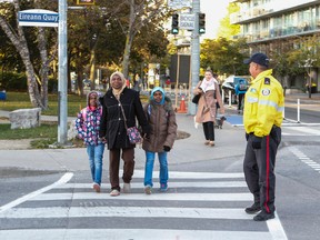 Toronto Police Const. Eddie O'Toole plays crossing guard at Queens Quay and Eireann Quay in Toronto as Hajia Abubaker crosses with her two daughters on their way to school Wednesday, October 26, 2016. (Dave Thomas/Toronto Sun)