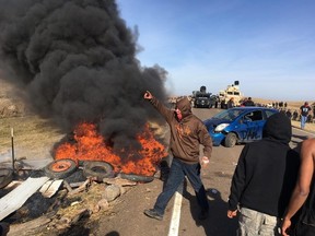 Demonstrators stand next to burning tires as armed soldiers and law enforcement officers assemble on Thursday, Oct. 27, 2016, to force them off private land where they had camped to block construction. (Mike McCleary/The Bismarck Tribune via AP)
