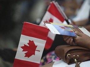 File photo - A woman holds a Canadian flag during a citizenship ceremony at Pearson International Airport on Monday June 30, 2014. Jack Boland/Toronto Sun/Postmedia Network