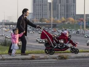 Mark Schmidt holds his daughter, Ava while pushing  Claudia in a stroller. Schmidt is angry his kids may have to navigate heavy traffic to get to school. (CRAIG ROBERTSON, Toronto Sun)