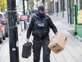 An officer carries evidence boxes as Ottawa police conduct raids on a number of pot shops including Wee Medical on Rideau St.  photo by Wayne Cuddington/ Postmedia