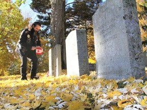 Daniel Chabot bends down to one the military graves on which to place Canadian flags in Cataraqui Cemetery in Kingston on Monday, part of a pre-Remembrance Day tradition. (Michael Lea/The Whig-Standard)
