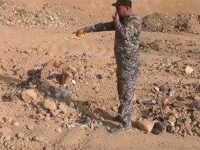 In this Monday, Nov. 7, 2016 frame grab from video, an Iraqi federal police officer holds his nose as he points towards a mass grave in Hamam al-Alil, Iraq. Investigators are probing the mass grave that was discovered the previous day by troops advancing further into Islamic State-held territory near the city of Mosul. Associated Press footage from the site shows bones and decomposed bodies among scraps of clothing and plastic bags dug out of the ground by a bulldozer after Iraqi troops noticed the strong smell while advancing into the town of Hamam al-Alil. (AP Photo)