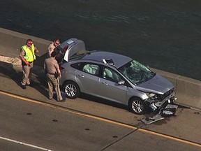 In this image provided by KGO-TV, police look over a car on the Benicia–Martinez left by a woman who jumped from the bridge Monday, Nov. 7, 2016, in Martinez, Calif. Police said a woman purposefully ran over her estranged husband and two of his friends in a crosswalk outside a family court and then jumped to her death off the bridge in the San Francisco Bay Area. (KGO-TV via AP)