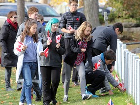 Students from a dozen schools in Kingston on Thursday fan out to place Canadian flags on the military graves in Cataraqui Cemetery prior to a pre-Remembrance Day service. (Michael Lea/The Whig-Standard)