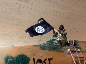 This undated image posted on Aug. 27, 2014 by the Raqqa Media Center of the Islamic State group, a Syrian opposition group, which has been verified and is consistent with other AP reporting, shows a fighter of the Islamic State group waving their flag from inside a captured government fighter jet following the battle for the Tabqa air base, in Raqqa, Syria. (AP Photo/ Raqqa Media Center of the Islamic State group)