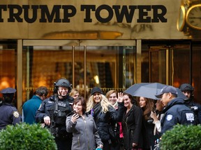 In this Nov. 15, 2016 file photo, a passersby stops for a selfie with a heavily-armed New York City police officer at the main, Fifth Avenue entrance to Trump Tower in New York. Outside Donald Trump's gilded skyscraper, many in the slow-moving sidewalk throng come for the sole purpose of snapping selfies, some to capture a bit of history and others to offer the new president their one-fingered salute. (AP Photo/Kathy Willens, File)