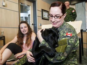 Ortona, National Service Dogs' "Puppy in Training," cuddles with his handler Capt. Donna Riguidel as her daughter, Darby Riguidel, 13, right, looks on at CFB Edmonton in Edmonton, Alta., on Monday, June 6, 2016. (Codie McLachlan/Postmedia)