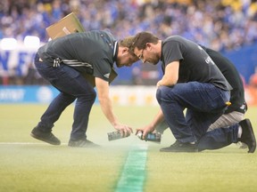 The grounds crew cover up a mis-painted line with spray paint, causing kickoff to be delayed by 40 minutes. (THE CANADIAN PRESS)
