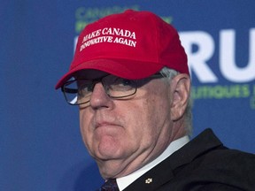 Former Industry minister and moderator John Manley puts on a red baseball cap as he jokes around before moderating a session with Innovation, Science and Economic Development Minister Navdeep Singh Bains at a conference in Ottawa, Wednesday October 12, 2016. Manley says Donald Trump's impending presidency poses an economic threat to Canada that's on par with the 9-11 attacks on the United States. (THE CANADIAN PRESS/Adrian Wyld)
