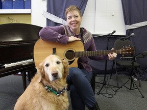 Shera Lumsden, director of MusicMates, an organization that helps children and adults with socialization through music, sits with her service dog Rocky in their building on Thursday. MusicMates is holding its first Christmas concert on Sunday. (Michael Lea/The Whig-Standard)