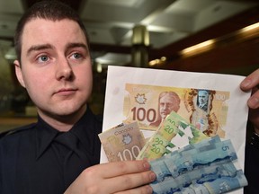 Const. Zachary Jansen holds up counterfeit  and altered currency as police have charged three suspects in relation to counterfeit money and warn retailers and consumers to be aware and how to spot a fake ones in Edmonton, Friday, November 25, 2016. Ed Kaiser/Postmedia