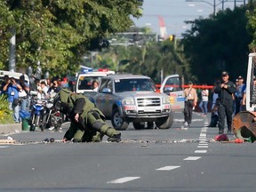 A Philippine National Police bomb disposal squad member, wearing a bomb-proof suit, leans to check the scene shortly after detonating in the middle of a boulevard, a suspicious package believed to be suspected IED or Improvised Explosive Device that was found in the trash bin near the U.S. Embassy in Manila, Philippines Monday, Nov. 28, 2016. (AP Photo/Bullit Marquez)