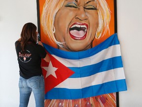 Suzanne Batlle, owner of the Azucar Ice Cream Company in Miami's Little Havana neighborhood, tapes a Cuban flag in front of a painting of Cuban singer Celia Cruz at her shop, Tuesday, Nov. 29, 2016. A large rally by Cuban exile groups is scheduled for Wednesday calling for change on the island in the wake of the death of Fidel Castro. (AP Photo/Wilfredo Lee)