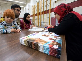 Esmaiel and Mariam Ejmili and their son, Alaa, chat with Maymona Ahmed, right, as she shows the new Londoners the City of London?s Spectrum programming guide at a Hello Neighbour event at Jean Vanier Catholic school. (CRAIG GLOVER, The London Free Press)