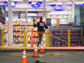 A Montreal police officer enters a convenience store at an Esso gas station where a woman was shot overnight. (Postmedia Network)