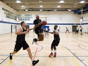 London Lightning player D'Vonne Pickett flies between players Taylor Black, left, and Jameel Williamson, right, as he shoots on the basket on the opening day of their basketball training camp at the YMCA Central Branch in London. (CRAIG GLOVER, The London Free Press)