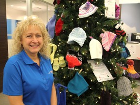 Kim Dunn, at the Bank of Montreal's Cataraqui Centre branch, in Kingston, Ont. on Friday, Dec. 2, 2016, stands next to their hat and mitt tree, on which people have been donating new or knitted items to be donated to the United Way. Dunn came up with the idea seven years ago. Michael Lea The Whig-Standard Postmedia Network