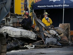 Crew workers walk behind debris from a warehouse fire in Oakland, Calif., Tuesday, Dec. 6, 2016. The fire erupted Friday, Dec. 2, 2016, killing dozens. (AP Photo/Jeff Chiu)