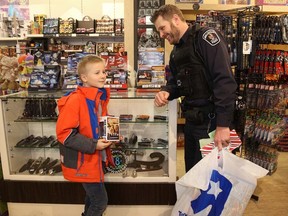 Cst. Darrell Hatfield, with 10-year-old Devon, waits in line to pay for a purchase at the Mind Games store in the Quinte Mall, during the Cop Shop event on Wednesday December 7, 2016 in Belleville, Ont. Emily Mountney-Lessard/Belleville Intelligencer/Postmedia Network