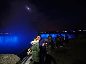 In this Saturday, Dec. 10, 2016 photo, people take a selfie near the Niagara Falls illuminated by new LED lights. (AP Photo/Julio Cortez)