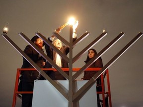 Rabbi Chaim Boyarsky, left, Rabbi Reuven Bulka and Abigail Freeman light a menorah at a Hanukkah celebration at city hall in Ottawa on Saturday, Dec. 24, 2016.