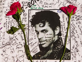 Flowers lie on a T-shirt signed by fans of singer Prince at a makeshift memorial place created outside the Apollo Theater in New York on April 22, 2016. The pop star died at the age of 57. (AP Photo/Andres Kudacki, File)