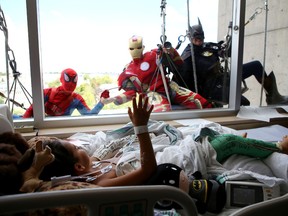 Luke Carter, 7, of Picton waves from his hospital bed to Spider-Man, Iron Man and Batman as they clean the windows of Connell 10 at Kingston General Hospital in Kingston, Ont. on Tuesday, Aug. 2, 2016. 
Elliot Ferguson/The Whig-Standard/Postmedia Network