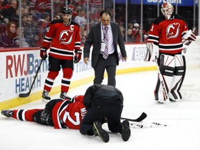 A trainer looks at Devils defenceman John Moore (2) after he suffered an injury during the first period against the Capitals in Newark, N.J., on Saturday, Dec. 31, 2016. Also seen are Devils' Andy Greene (6) and Keith Kinkaid (1). Moore was taken off the ice on a stretcher. (Julio Cortez/AP Photo)